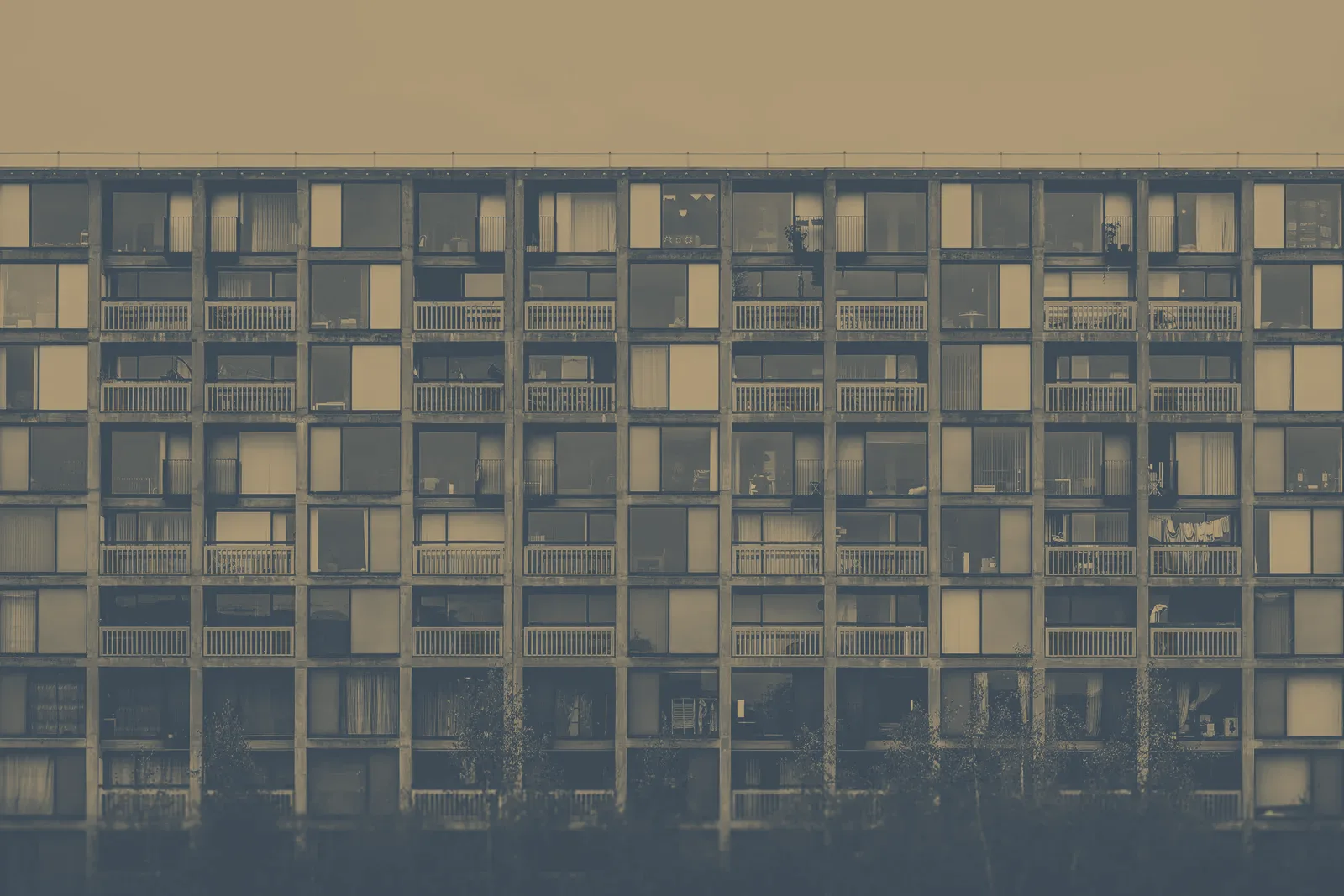 Façade d'un grand immeuble de logements en béton, avec ses rangées de fenêtres et de balcons, sous un ciel gris.