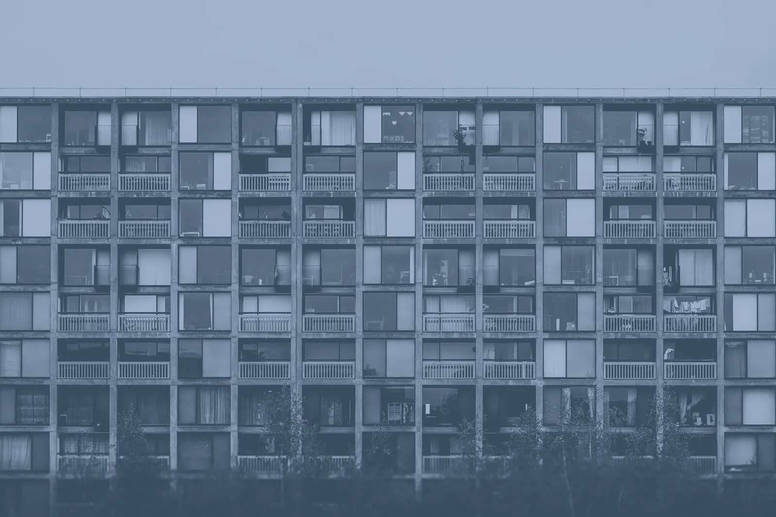 Façade d'un grand immeuble de logements en béton, avec ses rangées de fenêtres et de balcons, sous un ciel gris.
