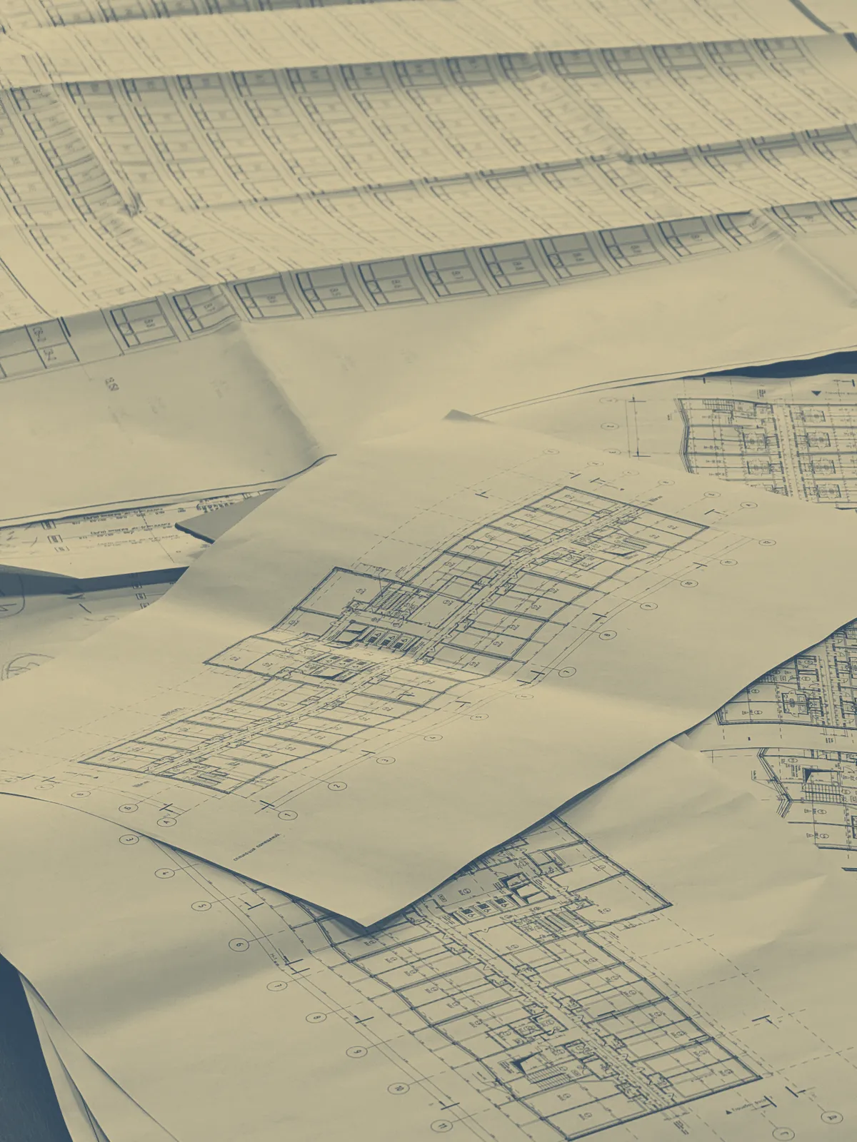 Plans techniques d'architecte étalés sur une table, en bichromie bleue et sable.